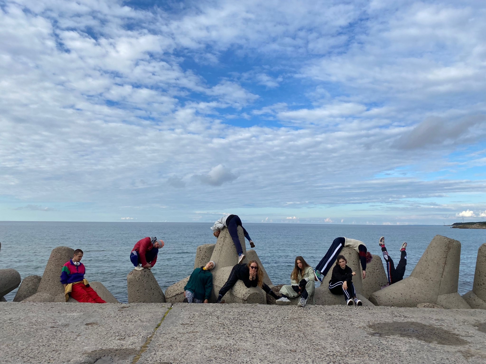Grupa ludzi stojących na betonowym falochronie nad morzem.