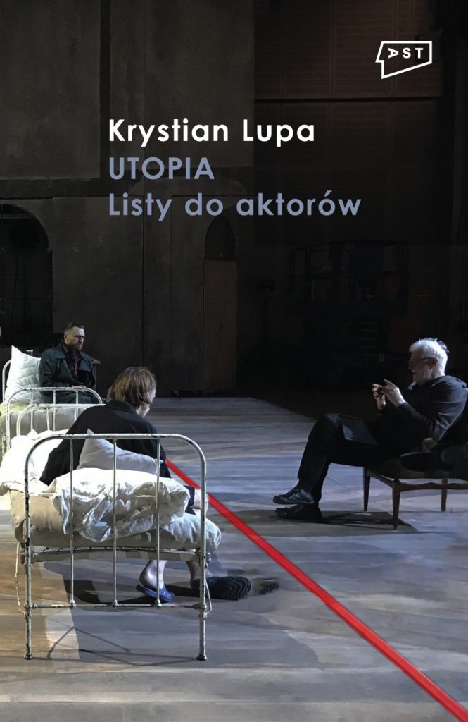 Okładka książki „Krystian Lupa. Utopia. Listy do aktorów". Fotografia z próby do spektaklu „Proces” Franza Kafki. Na scenie przedzielonej pośrodku czerwoną linią dwie postaci siedzące na starych, zniszczonych szpitalnych łóżkach. Naprzeciw nich siedzi reżyser Krystian Lupa