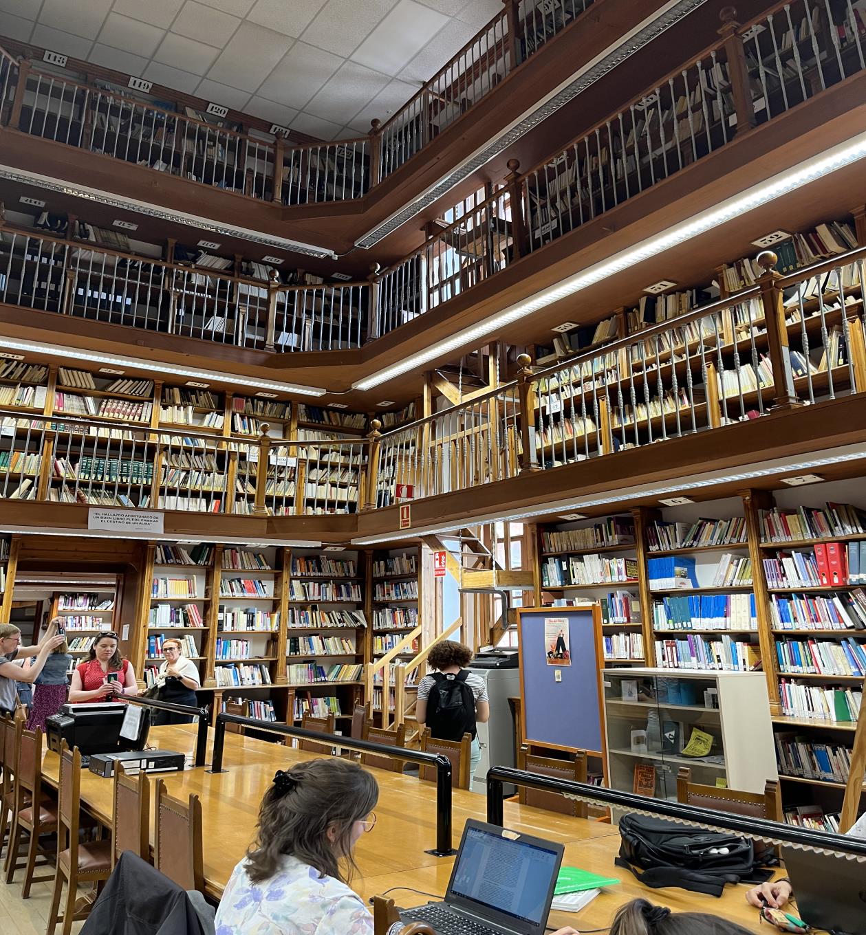 Tętniąca życiem biblioteka z mnóstwem książek i osobami siedzącymi przy stołach, zajętymi czytaniem i nauką.