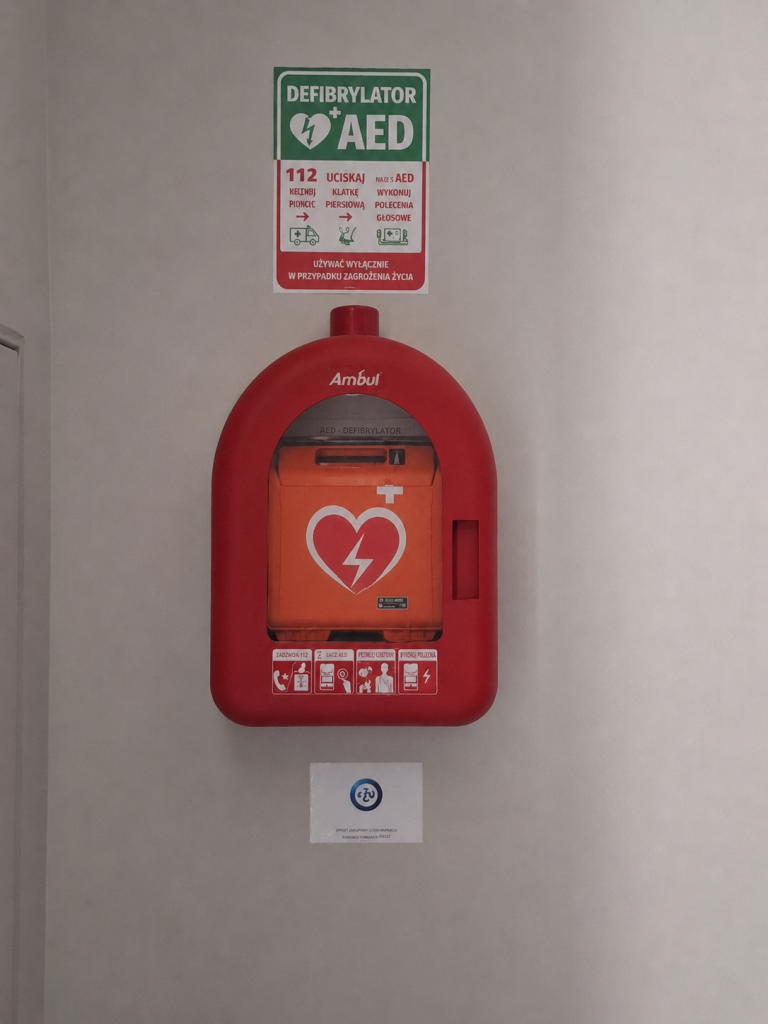 Czerwony defibrylator AED w szafce na jasnej ścianie.