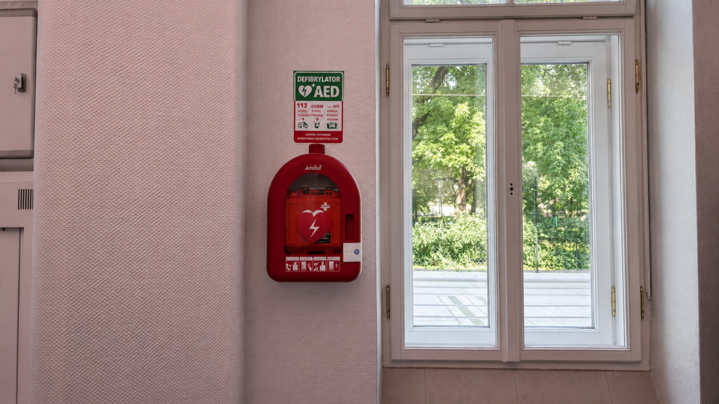 Czerwony defibrylator AED w szafce na ścianie po prawej stronie okna.
