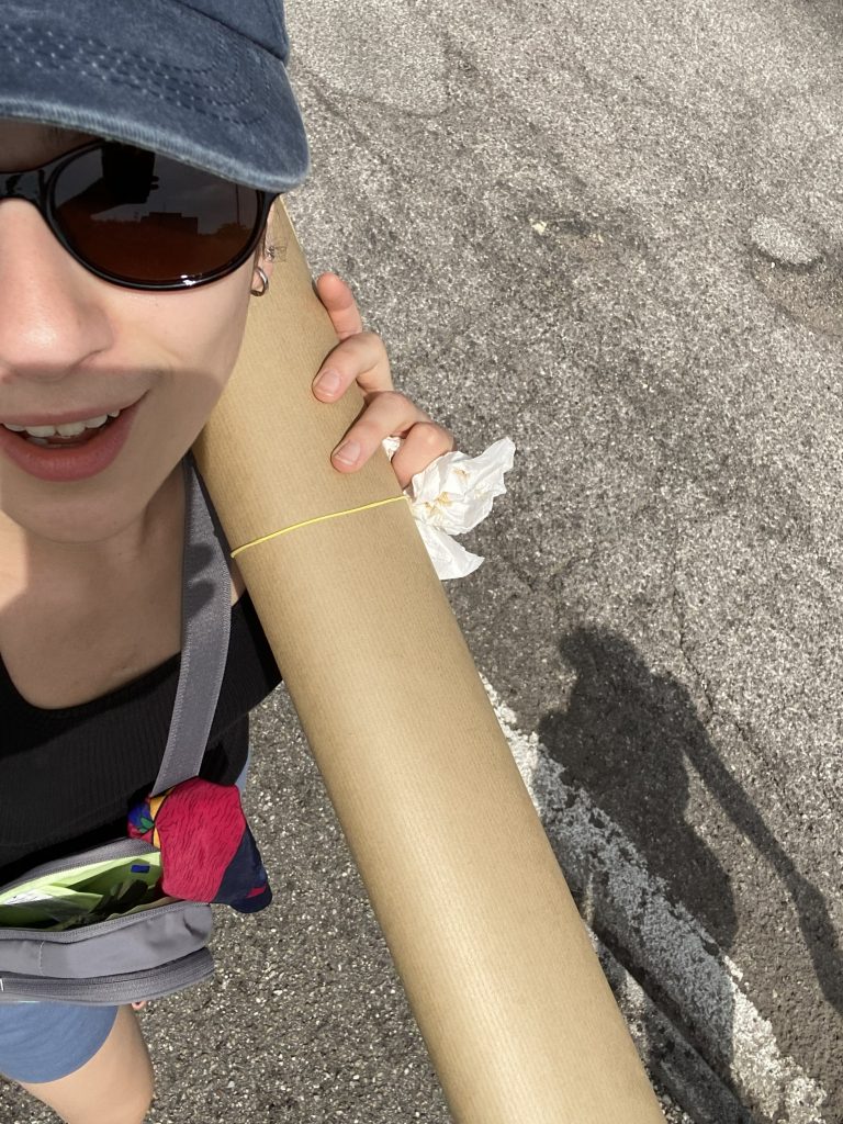 Selfie podróżniczki w czapce i okularach przeciwsłonecznych, trzymającej duży rulon papieru.