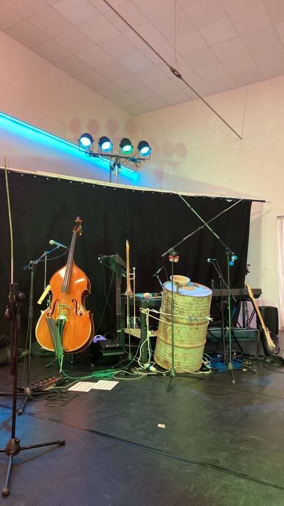 Scena przygotowana do koncertu, z kontrabasem, instrumentami, mikrofonami i metalową beczką.
