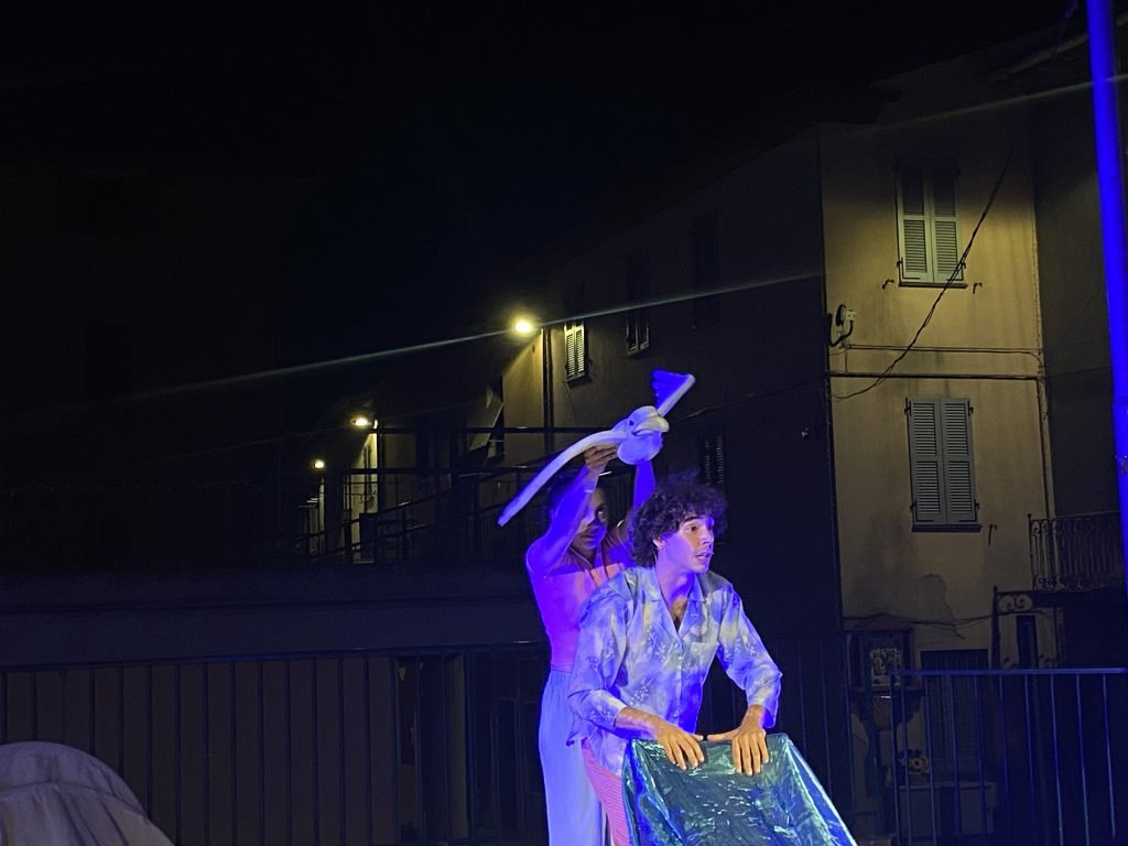 Dwoje artystów występujących nocą w plenerowym spektaklu, w niebieskim świetle ulicznym.