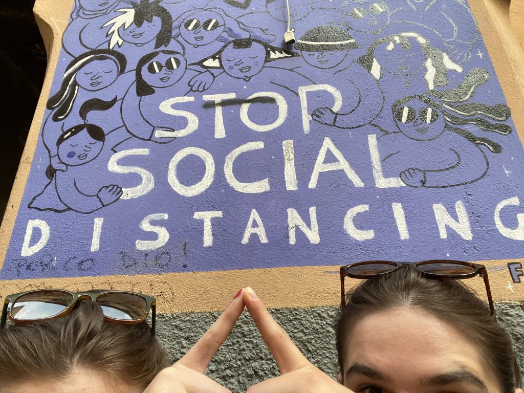 Fragment muralu z napisem „Stop social distancing”, postaciami oraz dłońmi dwóch osób.