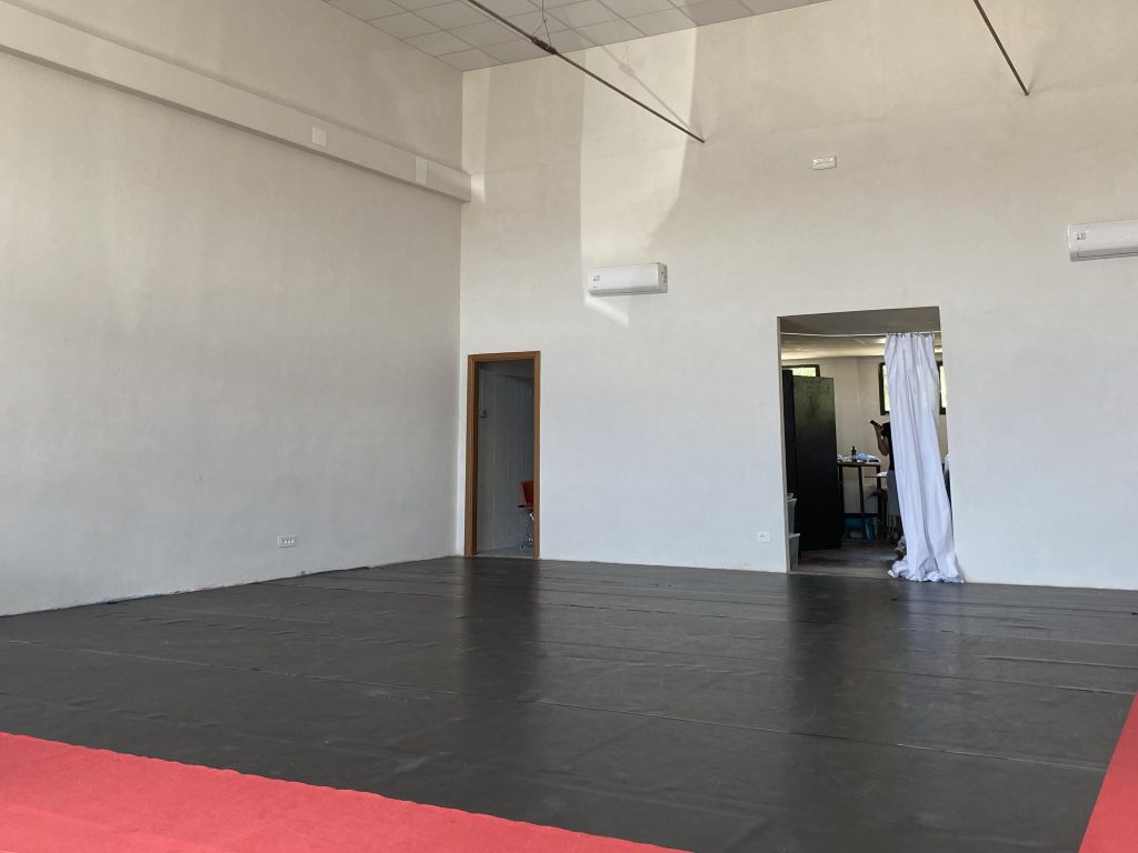 Pusta sala warsztatowa z czarną podłogą, białymi ścianami i czerwonym obrzeżem.