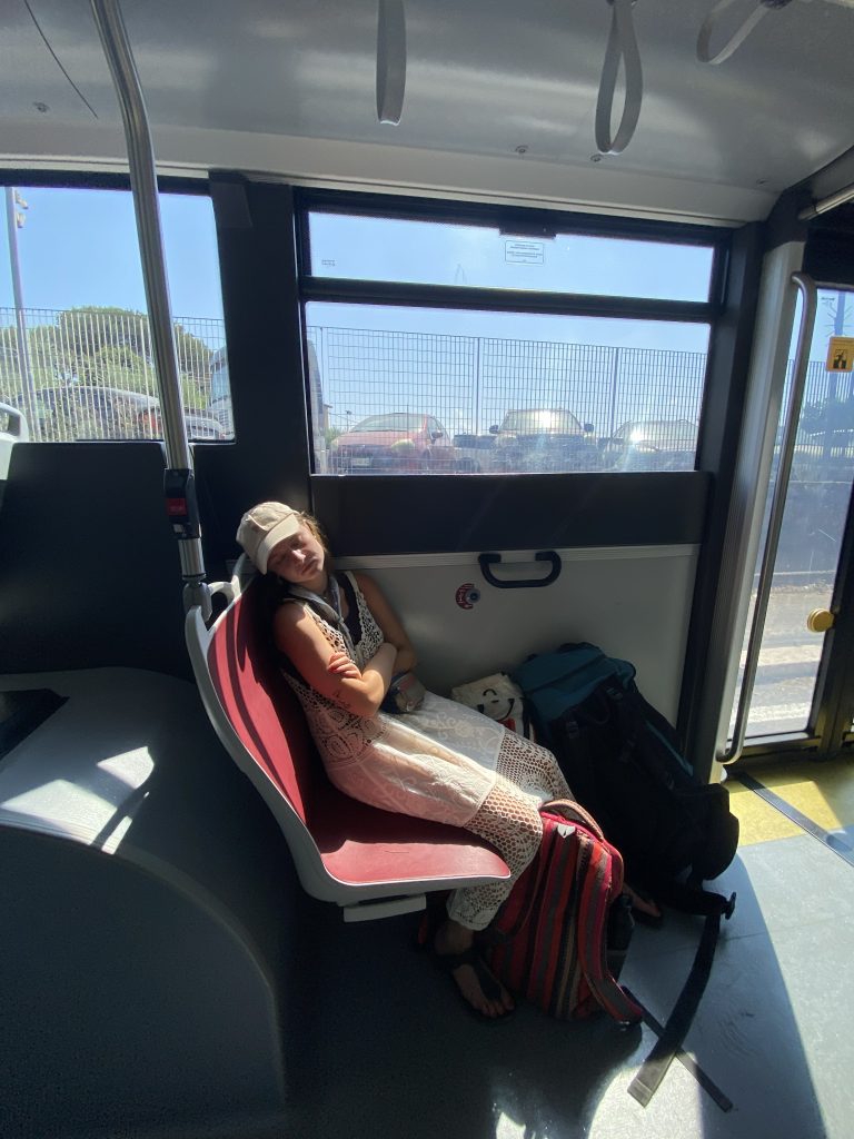 Osoba odpoczywająca na siedzeniu autobusu, z plecakami i bagażem ułożonym obok.