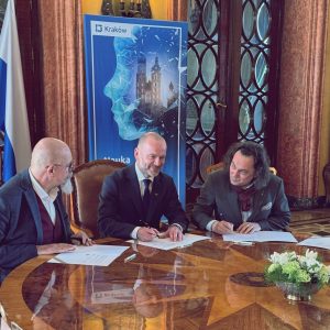 Rektorzy ASP, prof. Andrzej Bednarczyk, AST, dr hab. Grzegorz Mielczarek, prof. AST, AMKP, prof. Mariusz Sielski przy ozdobnym, drewnianym stole w zabytkowym wnętrzu, podpisują dokumenty.