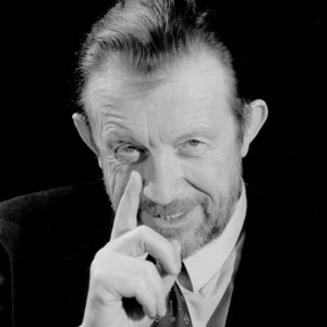 Czarno-biały portret Edwarda Linde-Lubaszenki, elegancko ubrany brodaty mężczyzna w średnim wieku o zaczesanych do tyłu włosach, trzymający prawą dłoń z wyciągniętym wskazującym palcem przy twarzy.